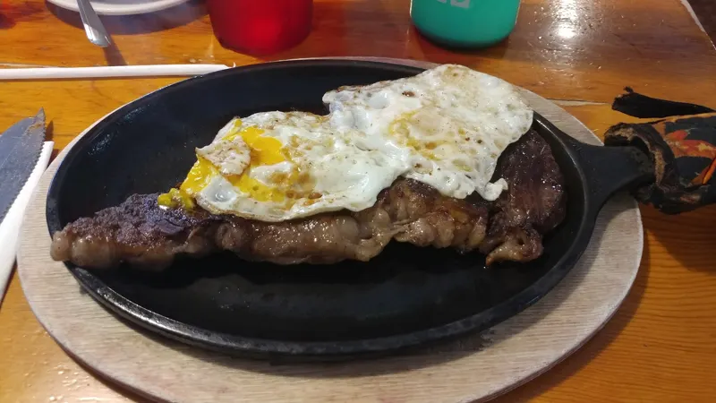 Steak topped with a fried egg on a sizzling skillet